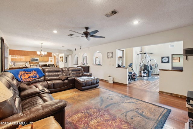 living room with a textured ceiling, light hardwood / wood-style floors, sink, and ceiling fan with notable chandelier