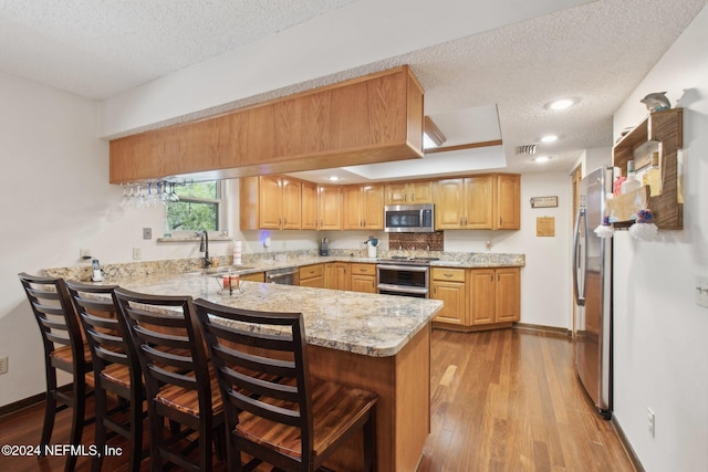 kitchen with kitchen peninsula, a textured ceiling, light wood-type flooring, and stainless steel appliances