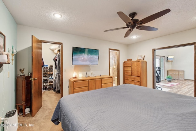 bedroom with a closet, light colored carpet, ceiling fan, a spacious closet, and a textured ceiling