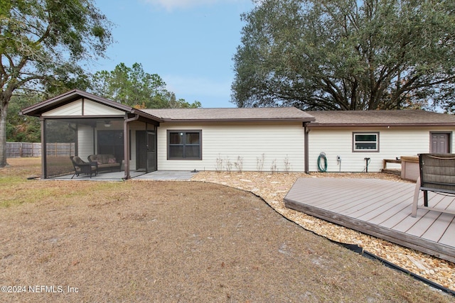 rear view of property featuring a lawn, a deck, and a sunroom