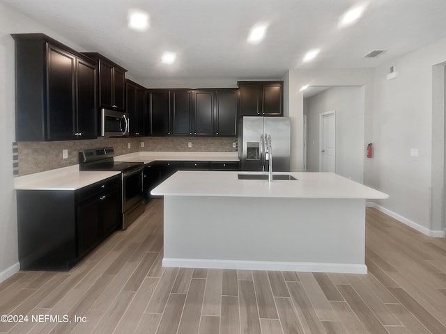 kitchen with appliances with stainless steel finishes, a center island with sink, and light hardwood / wood-style floors