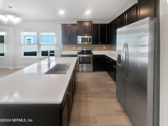 kitchen featuring sink, hanging light fixtures, light hardwood / wood-style floors, a center island with sink, and appliances with stainless steel finishes