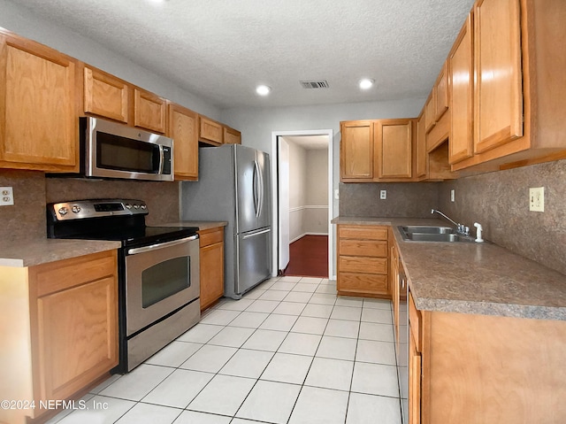 kitchen with sink, stainless steel appliances, a textured ceiling, decorative backsplash, and light tile patterned flooring