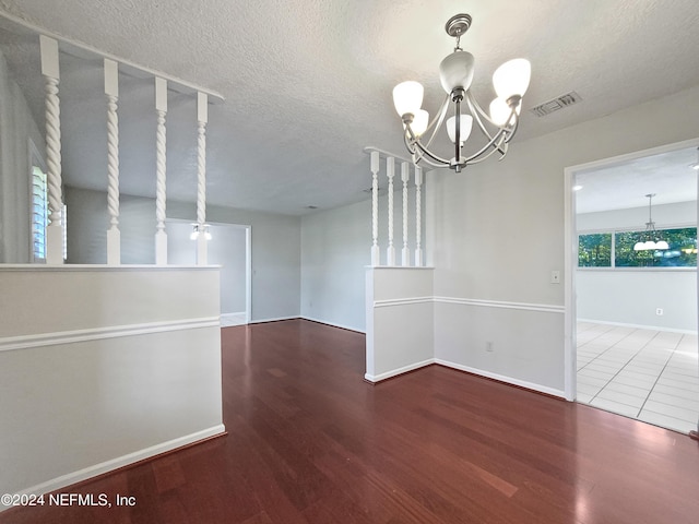 empty room featuring hardwood / wood-style floors, a textured ceiling, and a notable chandelier