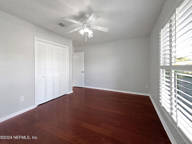 unfurnished bedroom featuring a textured ceiling, a closet, ceiling fan, and dark wood-type flooring