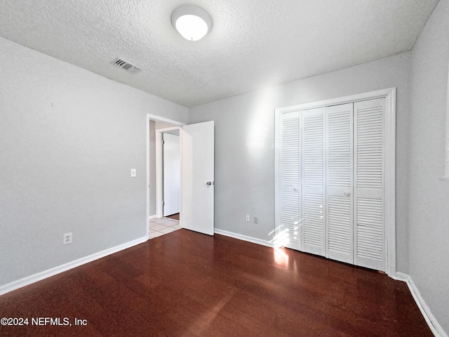 unfurnished bedroom with a closet, dark hardwood / wood-style floors, and a textured ceiling