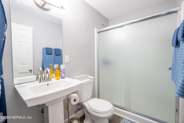 bathroom with hardwood / wood-style floors, toilet, a shower with shower door, and a textured ceiling