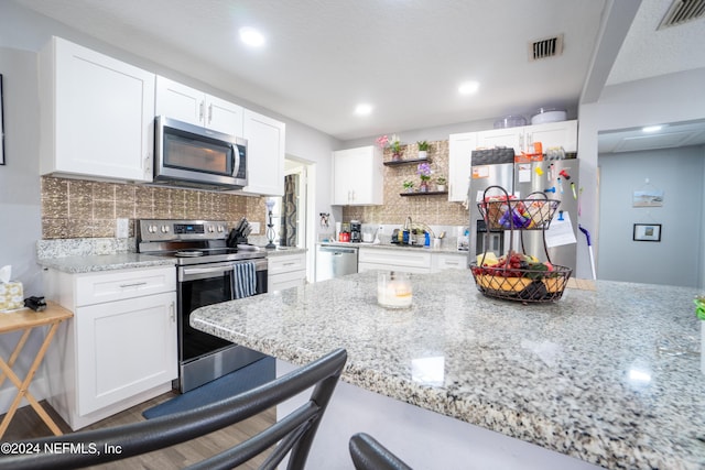 kitchen with light stone countertops, tasteful backsplash, a breakfast bar, stainless steel appliances, and white cabinets