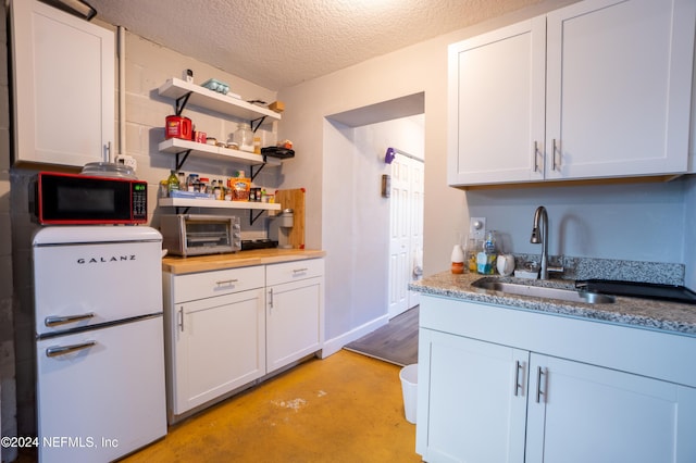 kitchen with sink, white cabinets, white fridge, and a textured ceiling