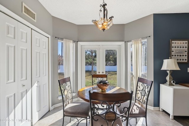 tiled dining space with french doors, a textured ceiling, plenty of natural light, and a notable chandelier