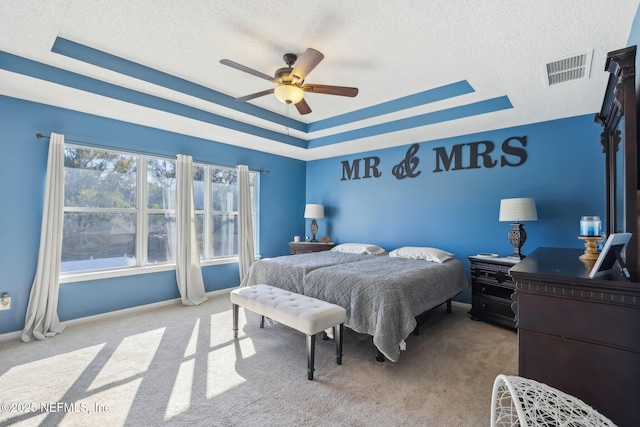 carpeted bedroom featuring ceiling fan, a raised ceiling, and a textured ceiling