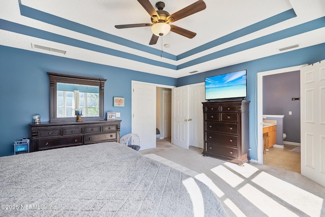 carpeted bedroom with ensuite bathroom, a raised ceiling, and ceiling fan