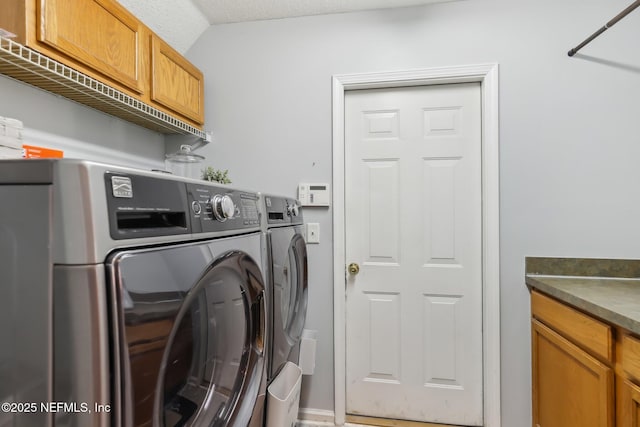 clothes washing area with washing machine and clothes dryer, cabinets, and a textured ceiling