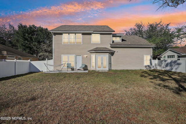 back house at dusk featuring a lawn, a patio, and french doors