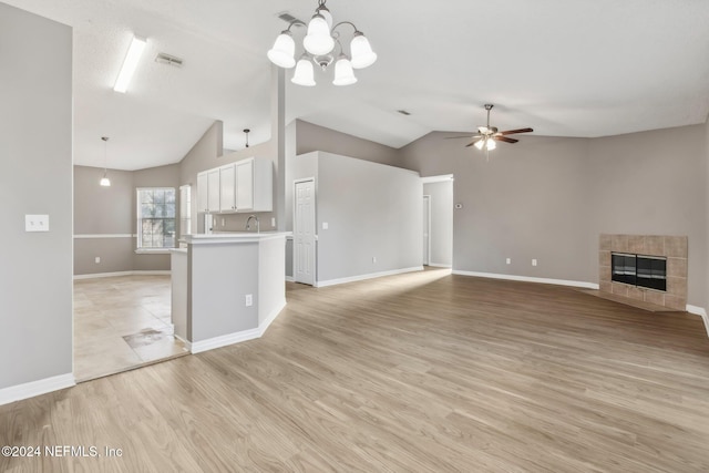 unfurnished living room featuring vaulted ceiling, a tiled fireplace, ceiling fan with notable chandelier, and light wood-type flooring