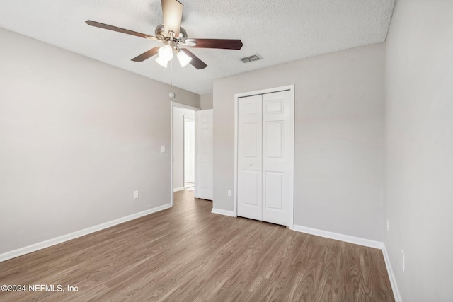 unfurnished bedroom with ceiling fan, light wood-type flooring, a textured ceiling, and a closet