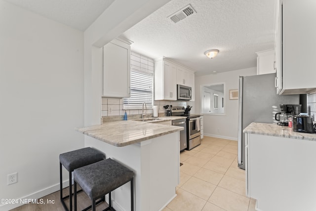 kitchen featuring sink, white cabinetry, light stone counters, appliances with stainless steel finishes, and a kitchen breakfast bar