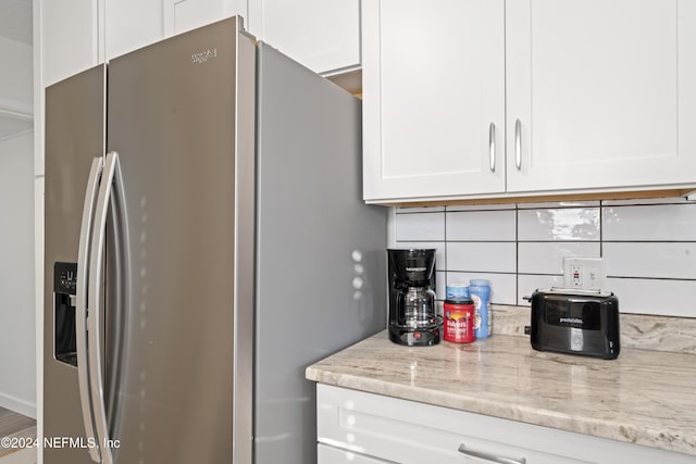 kitchen with white cabinetry, stainless steel refrigerator with ice dispenser, light stone countertops, and decorative backsplash