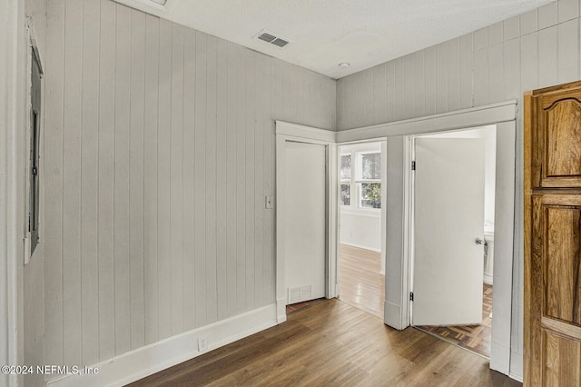 spare room with wood-type flooring, a textured ceiling, and wooden walls