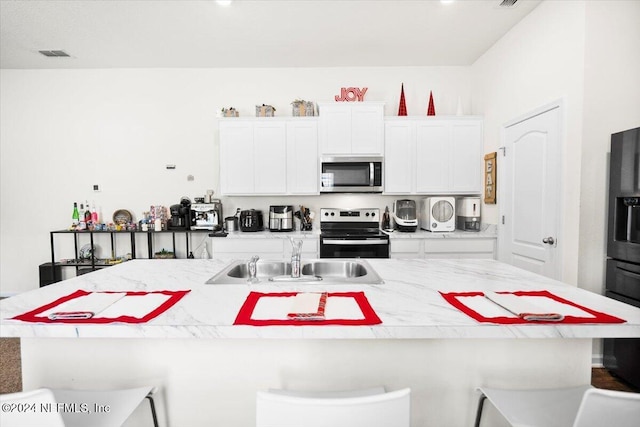 kitchen with appliances with stainless steel finishes, a kitchen breakfast bar, sink, a center island with sink, and white cabinets