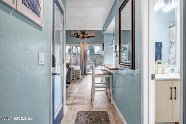 hallway featuring sink, a chandelier, and light wood-type flooring