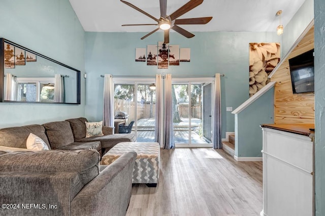 living room with ceiling fan, light hardwood / wood-style flooring, and a high ceiling