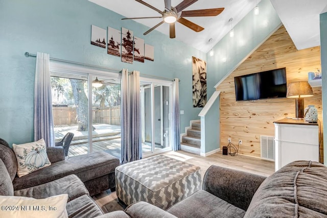 living room featuring wood walls, light hardwood / wood-style flooring, high vaulted ceiling, and ceiling fan