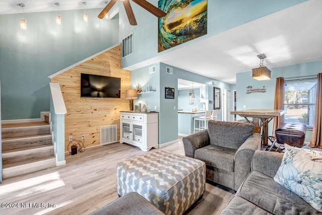 living room featuring ceiling fan, wood walls, light hardwood / wood-style floors, and high vaulted ceiling