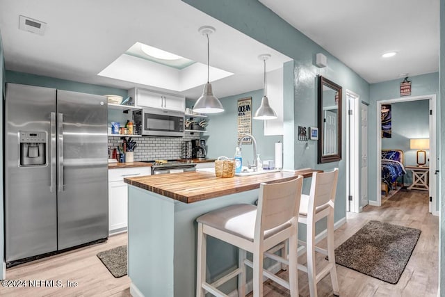 kitchen featuring appliances with stainless steel finishes, pendant lighting, light hardwood / wood-style flooring, white cabinets, and butcher block counters