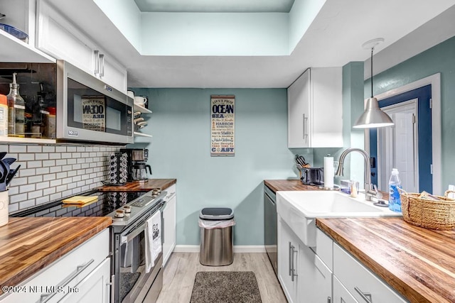 kitchen with wooden counters, light wood-type flooring, stainless steel appliances, pendant lighting, and white cabinetry