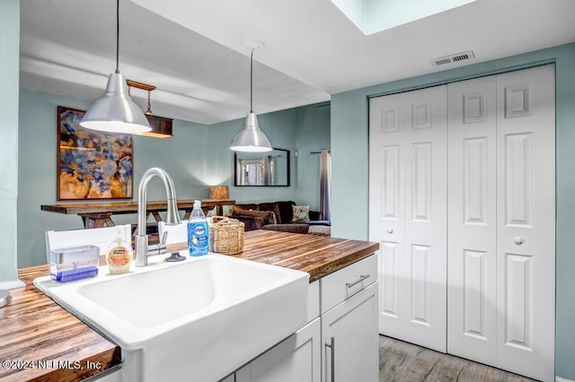 kitchen featuring wooden counters, sink, white cabinets, light hardwood / wood-style floors, and hanging light fixtures