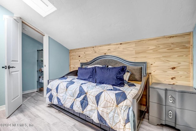 bedroom with vaulted ceiling with skylight, wood walls, and hardwood / wood-style flooring