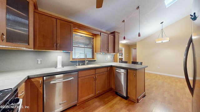 kitchen featuring kitchen peninsula, vaulted ceiling with skylight, stainless steel appliances, sink, and hanging light fixtures