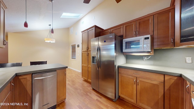 kitchen with appliances with stainless steel finishes, light wood-type flooring, pendant lighting, and vaulted ceiling with skylight