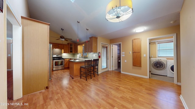 kitchen with hanging light fixtures, a kitchen breakfast bar, separate washer and dryer, vaulted ceiling, and stainless steel stove