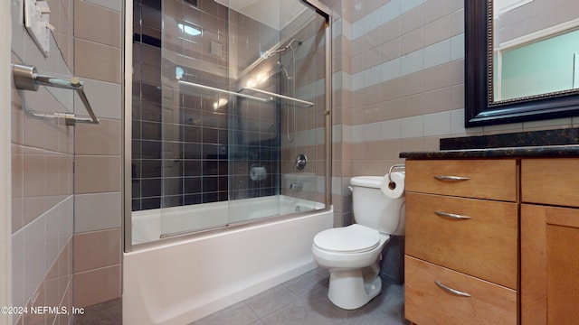 full bathroom with vanity, tile patterned floors, bath / shower combo with glass door, toilet, and tile walls