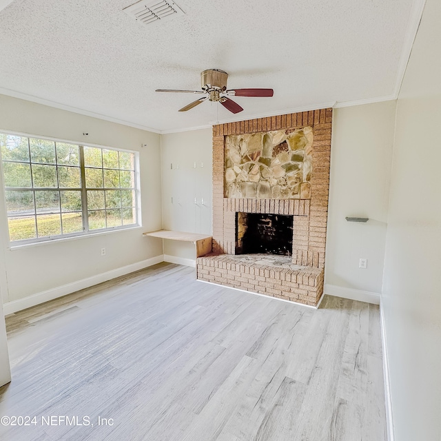 unfurnished living room with a textured ceiling, ceiling fan, crown molding, a fireplace, and light hardwood / wood-style floors