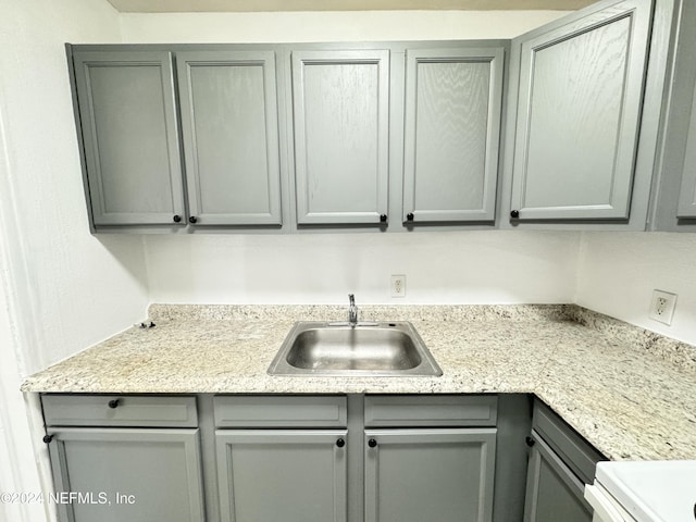 kitchen with gray cabinetry, light stone counters, and sink