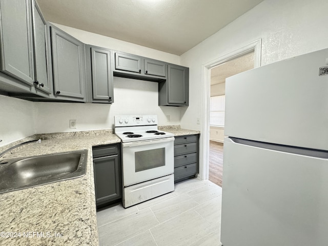 kitchen featuring gray cabinetry, white appliances, sink, light stone countertops, and light wood-type flooring