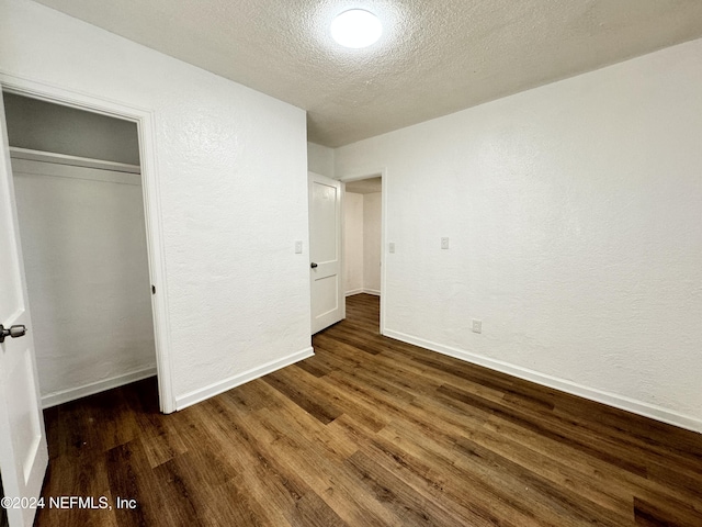 unfurnished bedroom with a textured ceiling, a closet, and dark wood-type flooring