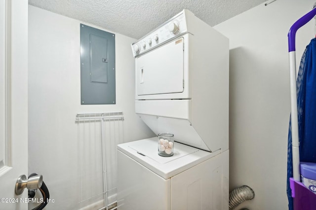 washroom with a textured ceiling, electric panel, and stacked washer / drying machine