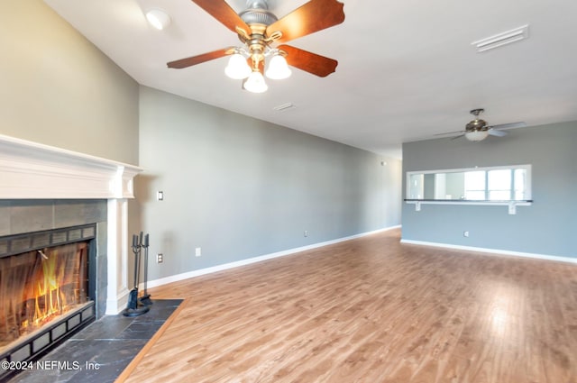 unfurnished living room featuring a tiled fireplace, ceiling fan, and hardwood / wood-style floors