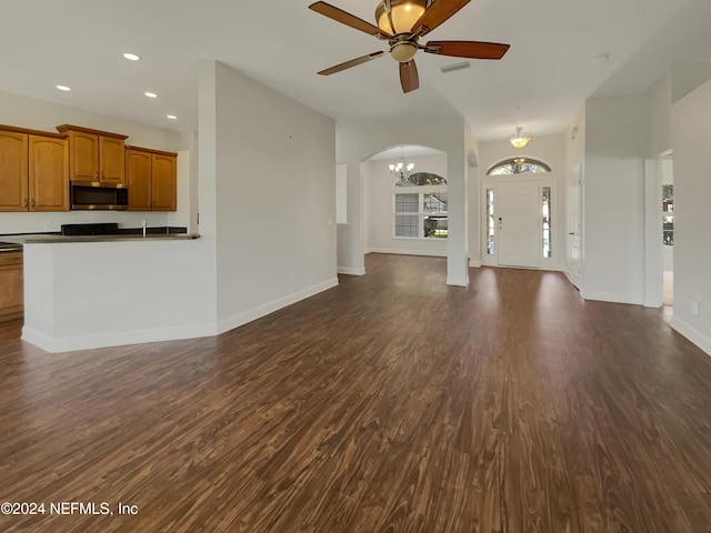 unfurnished living room featuring ceiling fan with notable chandelier and dark wood-type flooring