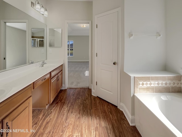 bathroom with hardwood / wood-style floors, vanity, and tiled bath