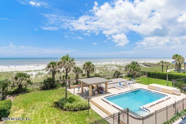 view of swimming pool with a lawn, a water view, a patio, and a view of the beach