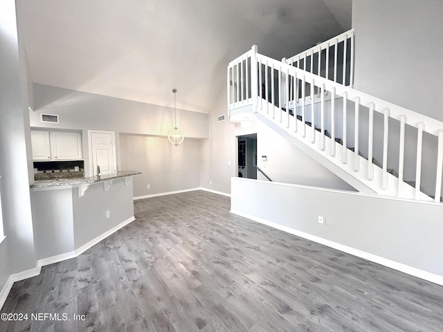 unfurnished living room with dark wood-type flooring, high vaulted ceiling, and a chandelier