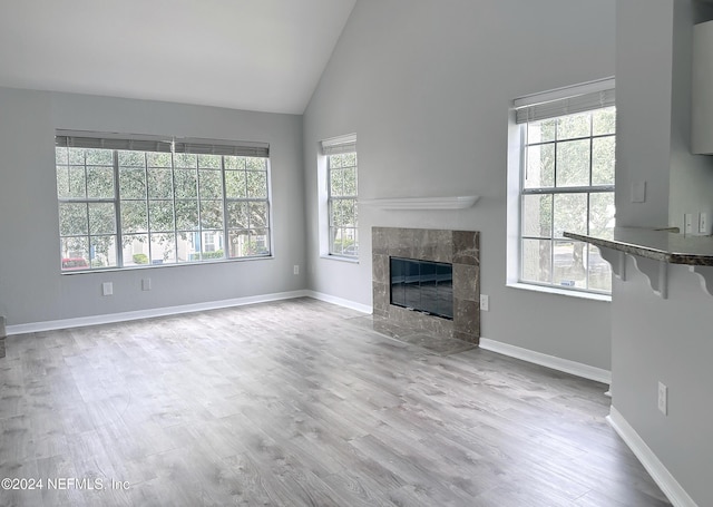 unfurnished living room with a tile fireplace, plenty of natural light, high vaulted ceiling, and light wood-type flooring