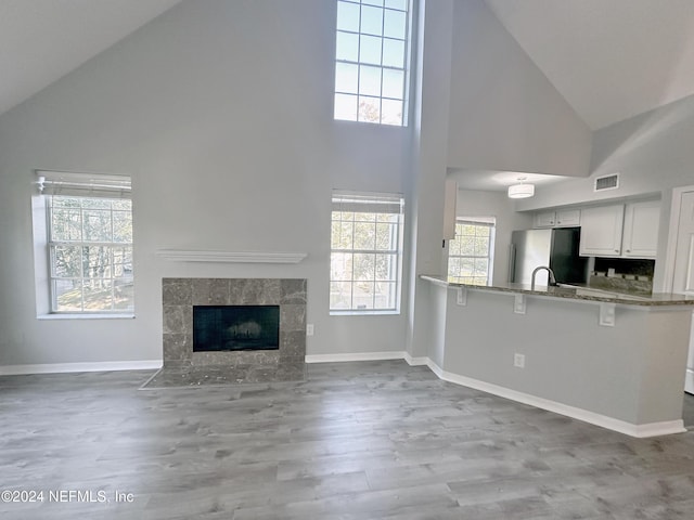 kitchen featuring stainless steel refrigerator, high vaulted ceiling, kitchen peninsula, a fireplace, and white cabinets