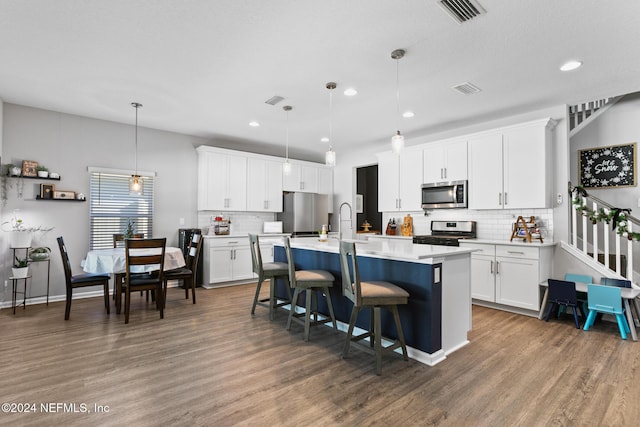 kitchen featuring dark wood-type flooring, white cabinets, a center island with sink, hanging light fixtures, and appliances with stainless steel finishes