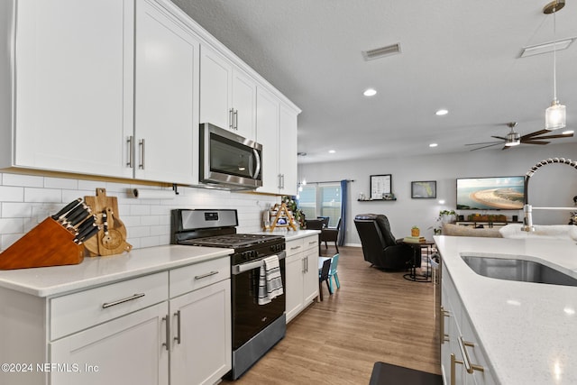 kitchen featuring white cabinets, light wood-type flooring, stainless steel appliances, and hanging light fixtures